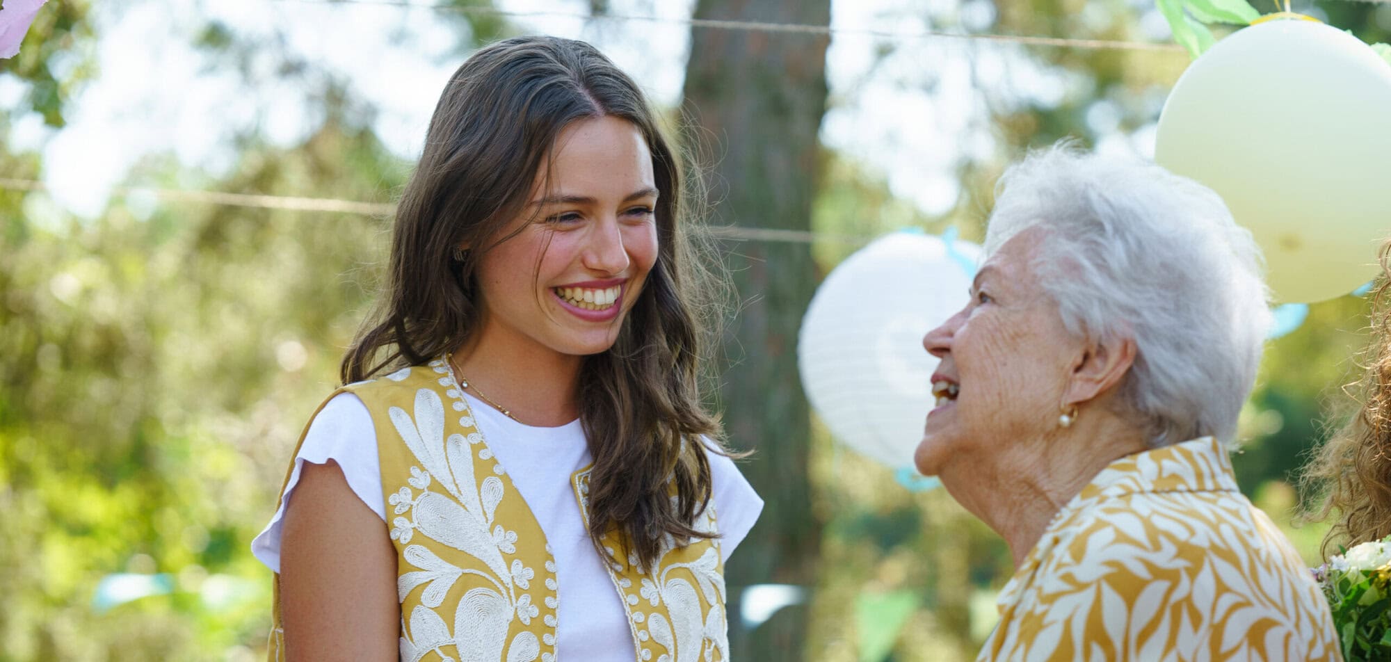 Mature granddaughter and grandmother reunite after a long time, talking. Family gathering at a garden party. Banner with copy space. UK pension changes make it easier for your family when you have a will in place.
