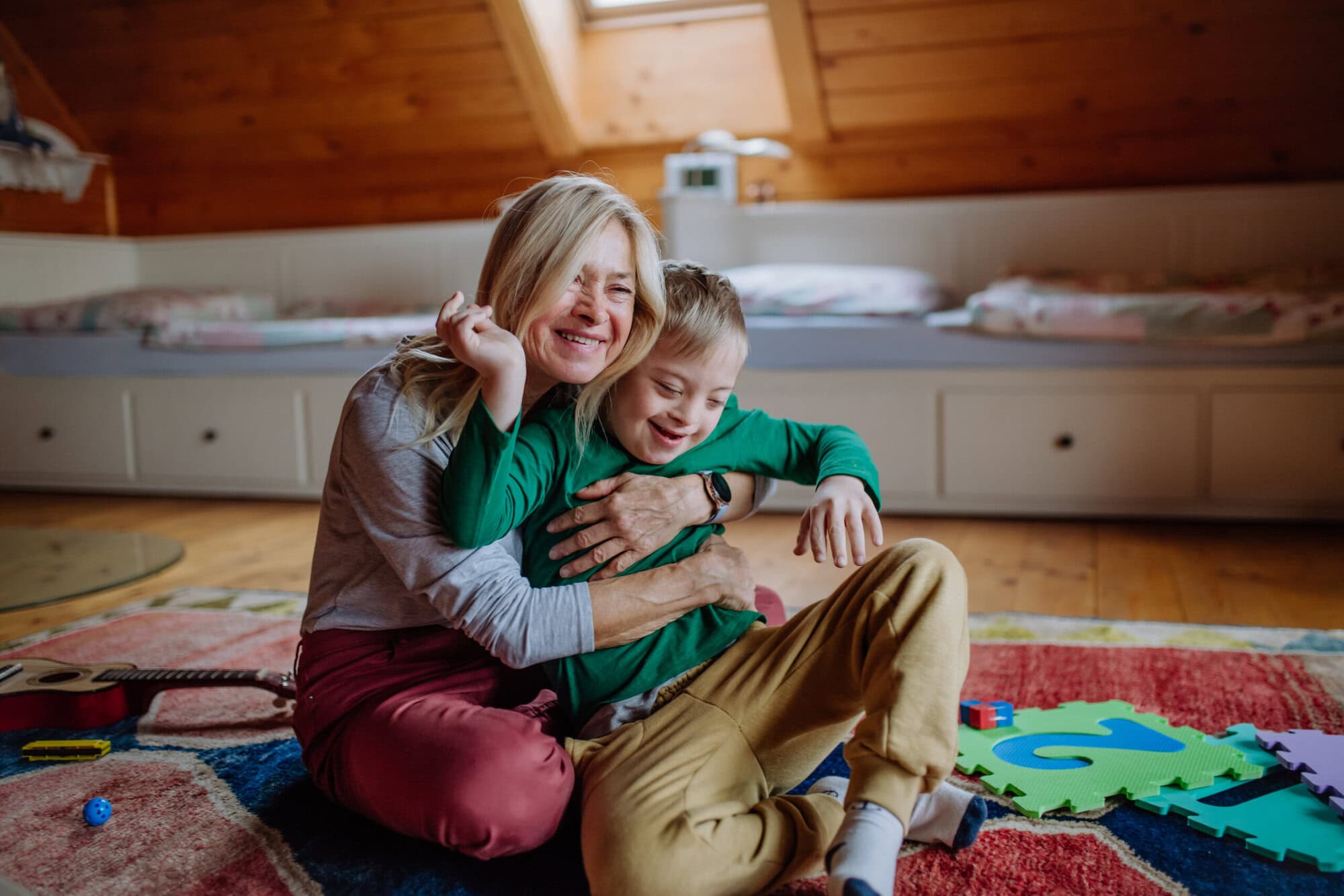 Happy boy with Down syndrome sitting on floor and hugging with his grandmother at home. Combine Disability Trusts with State Benefits to protect beneficiaries.