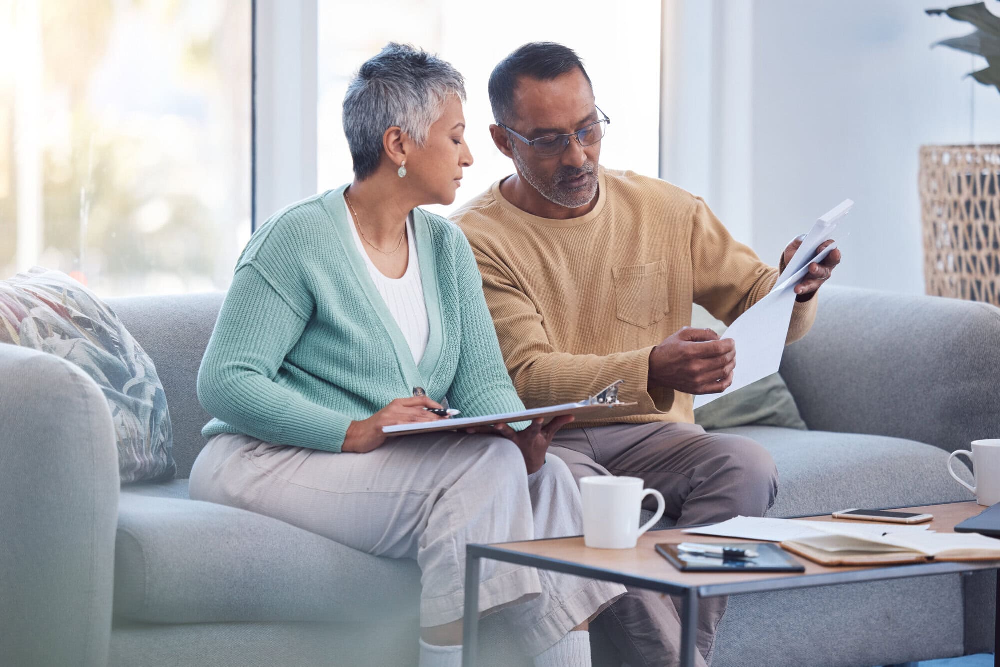 Finance, documents and senior couple on sofa with bills, paperwork and insurance checklist in home, life or asset management, Elderly black people on couch with financial, retirement or mortgage debt De-listed QROPS can affect your retirement savings.