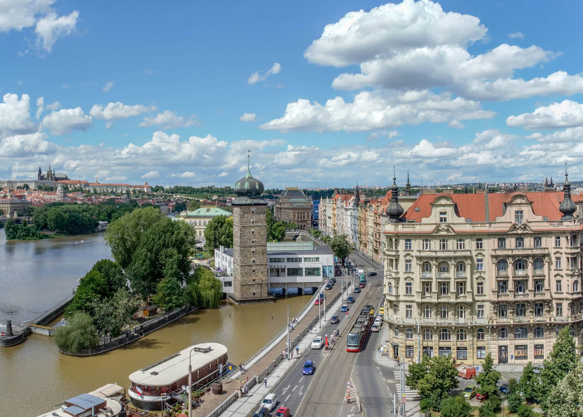 View of the new Prague. Near the tower, Vltava with ships. Tram rides on the street. Beautiful and historic buildings. Great view and idea for traveling to the Czech Republic. "Europoor" term does not describe the Czech Republic